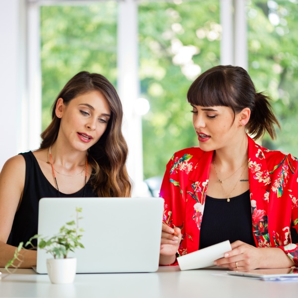 Two women sitting at a table looking at a laptop