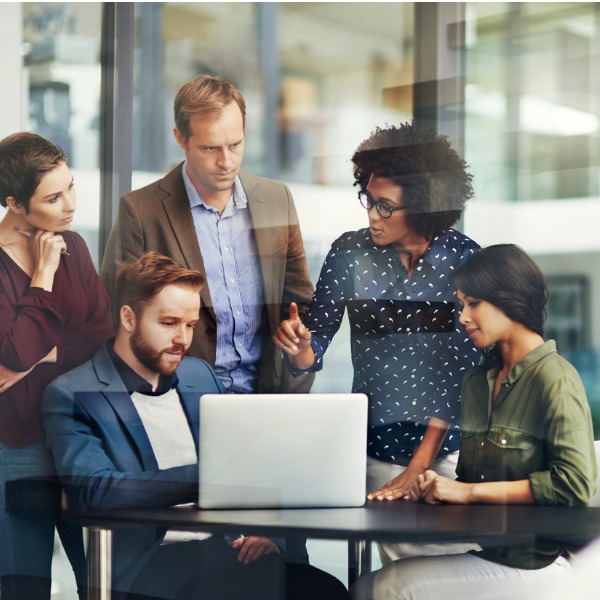 Group of professionals sitting and standing around a table with a laptop open