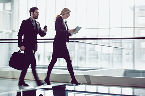 One man and one woman business professional walking at a fast pace in an office