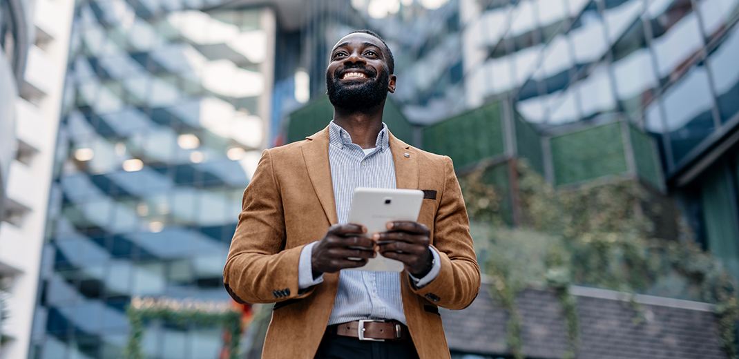 Man in front of building smiling and holding tablet