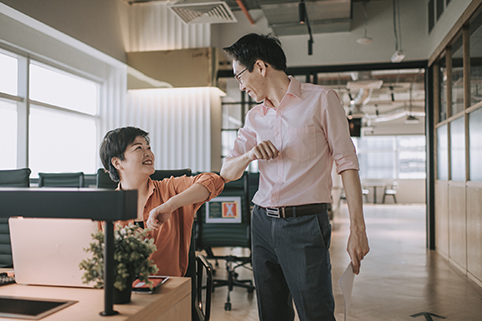 Two colleagues bumping elbows in the office