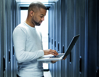 Man standing in a data center holding an open laptop
