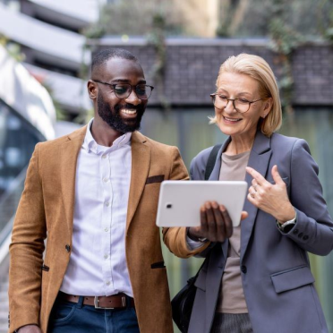 Man and woman smiling while looking at tablet outdoors